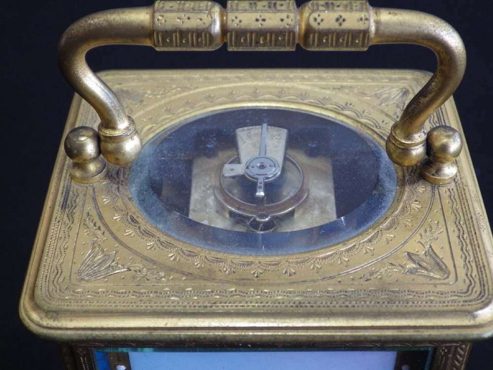An engraved brass French carriage clock featuring a carrying handle, white enamel Roman numeral dial, and a hand-painted landscape panel. View IX