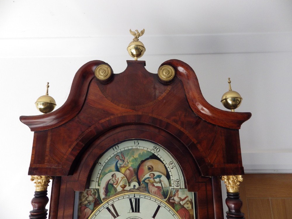 An antique flame mahogany longcase clock featuring a painted dial, swan-neck pediment with brass finials, and spirally turned column detailing. View II