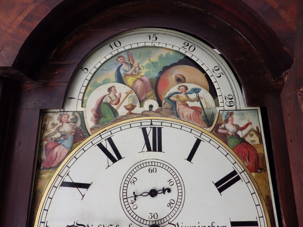 An antique flame mahogany longcase clock featuring a painted dial, swan-neck pediment with brass finials, and spirally turned column detailing. View III