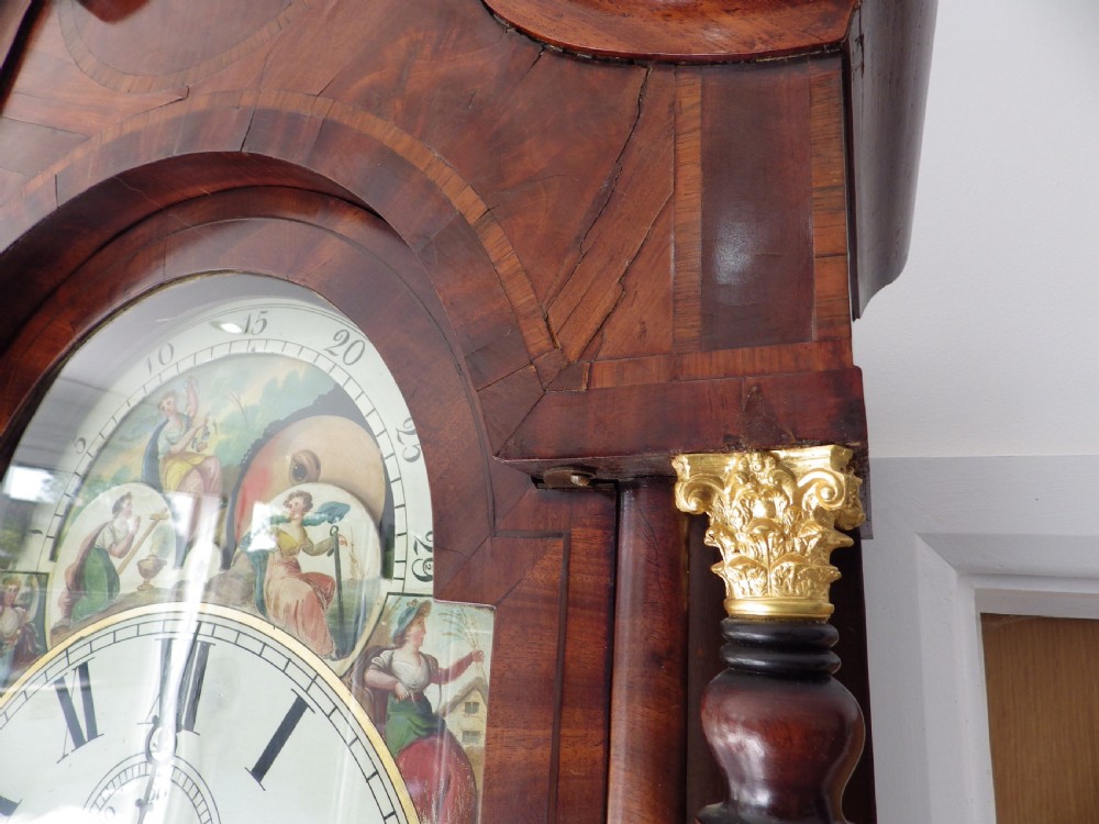 An antique flame mahogany longcase clock featuring a painted dial, swan-neck pediment with brass finials, and spirally turned column detailing. View V