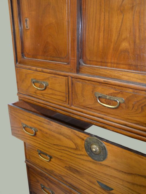 fig 2. A tall Taisho period Japanese elm tansu chest featuring prominent wood grain, circular brass escutcheons, sliding top cabinet doors, and multiple drawers.
