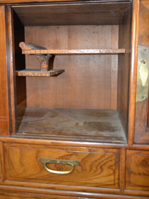 fig 3. A tall Taisho period Japanese elm tansu chest featuring prominent wood grain, circular brass escutcheons, sliding top cabinet doors, and multiple drawers.