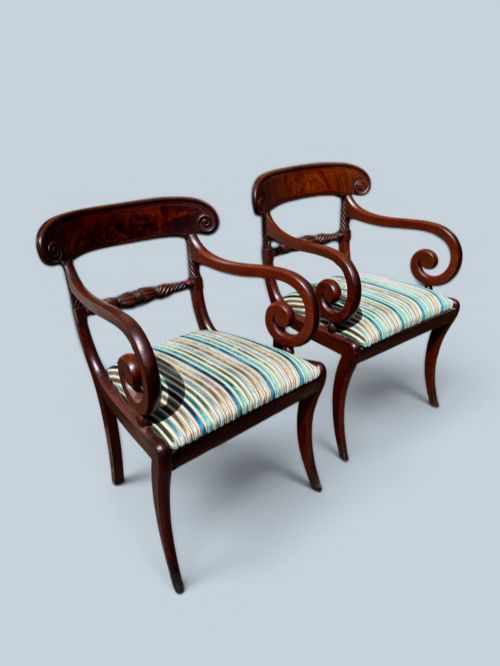 fig 1. A pair of antique Regency mahogany armchairs featuring curved scroll arms, striped velvet seats, and sabre legs.