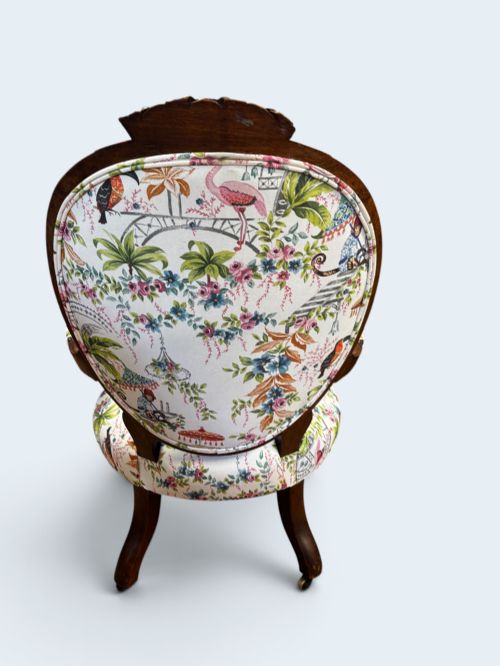 fig 2. A Victorian carved mahogany armchair featuring an oval button-backed backrest, padded armrests, and botanical floral upholstery set on cabriole legs with brass castors.
