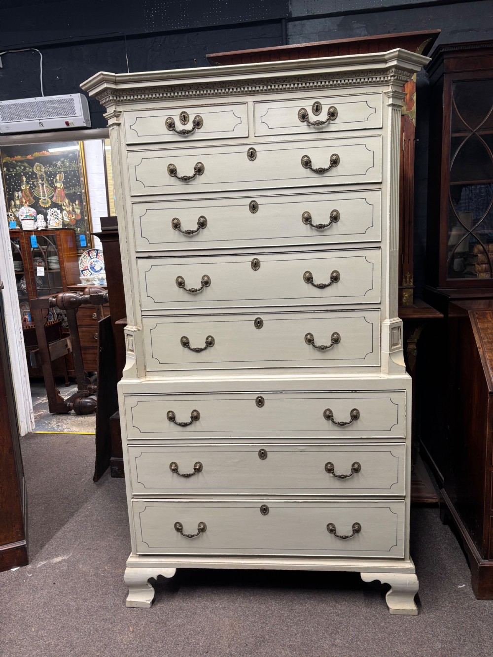 A tall cream-painted Georgian chest-on-chest featuring brass swan-neck handles, dentil moulding cornice, blue line detailing, and bracket feet. View V