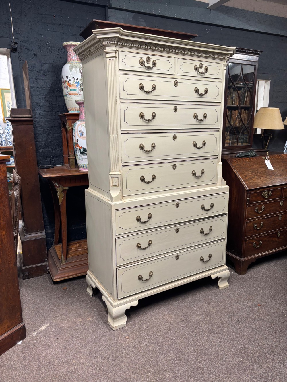 A tall cream-painted Georgian chest-on-chest featuring brass swan-neck handles, dentil moulding cornice, blue line detailing, and bracket feet. View VII