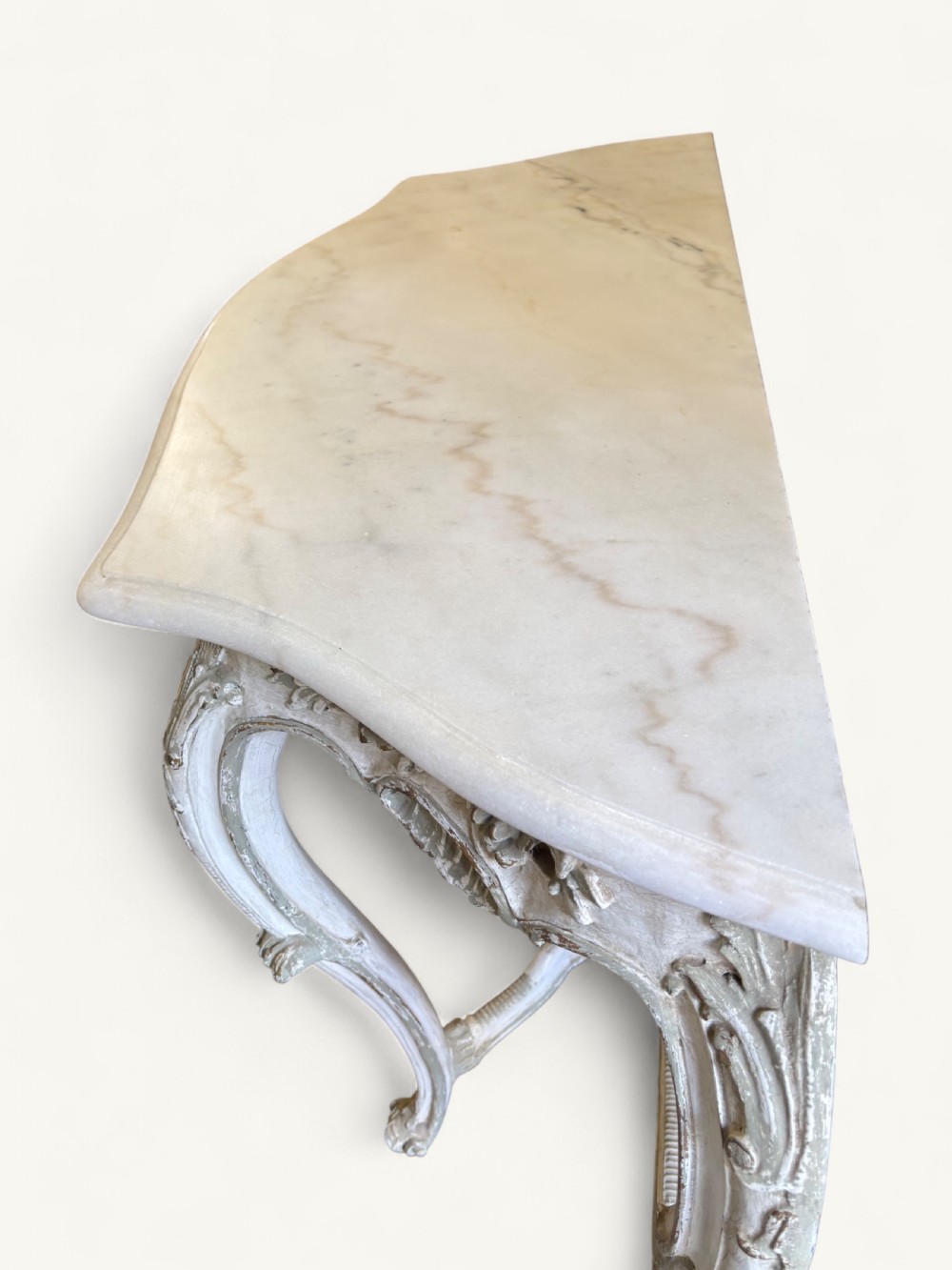 A French Rococo style console table featuring a light marble top, off-white distressed paint finish, cabriole legs, and an intricately carved apron with scrolls. View VIII