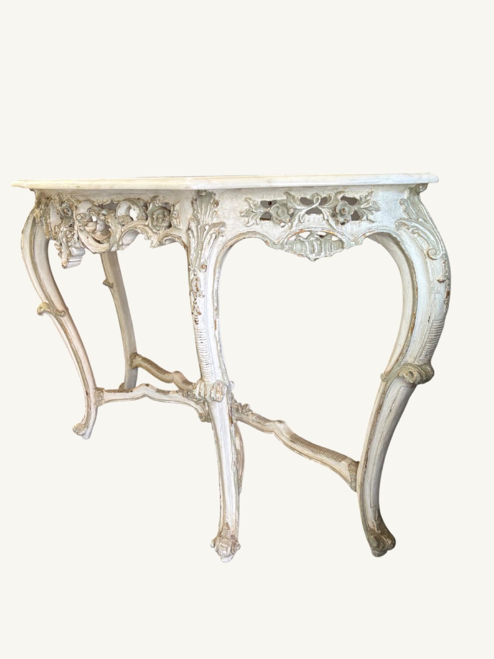 A French Rococo style console table featuring a light marble top, off-white distressed paint finish, cabriole legs, and an intricately carved apron with scrolls. View IX