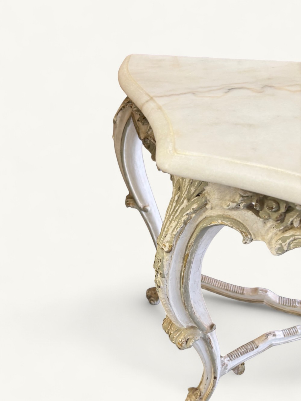 A French Rococo style console table featuring a light marble top, off-white distressed paint finish, cabriole legs, and an intricately carved apron with scrolls. View X