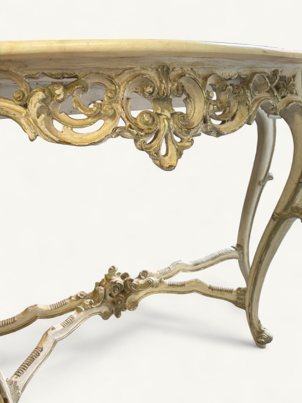 A French Rococo style console table featuring a light marble top, off-white distressed paint finish, cabriole legs, and an intricately carved apron with scrolls. View XII