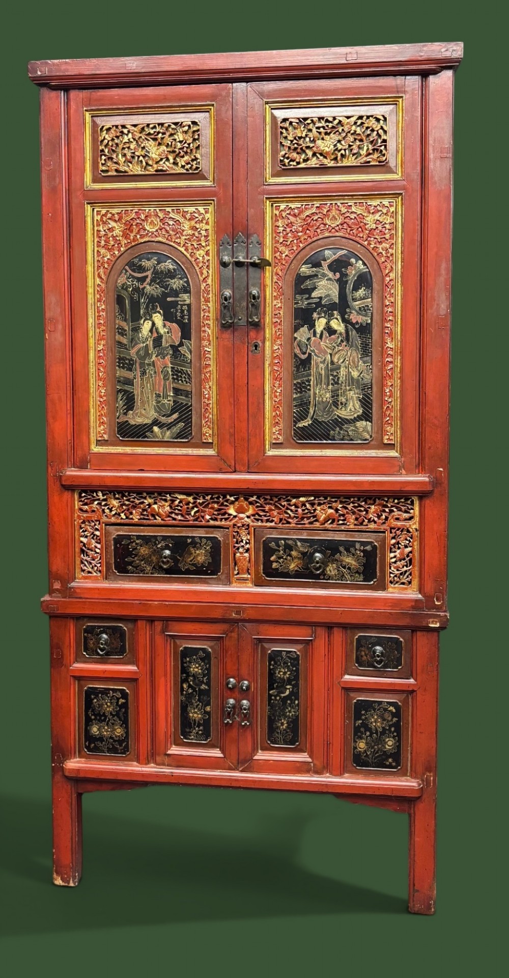 An antique Chinese tall wooden cabinet featuring red lacquered framing, gilded openwork wood carvings, black panels decorated with gold figures and floral motifs, and central brass hardware.