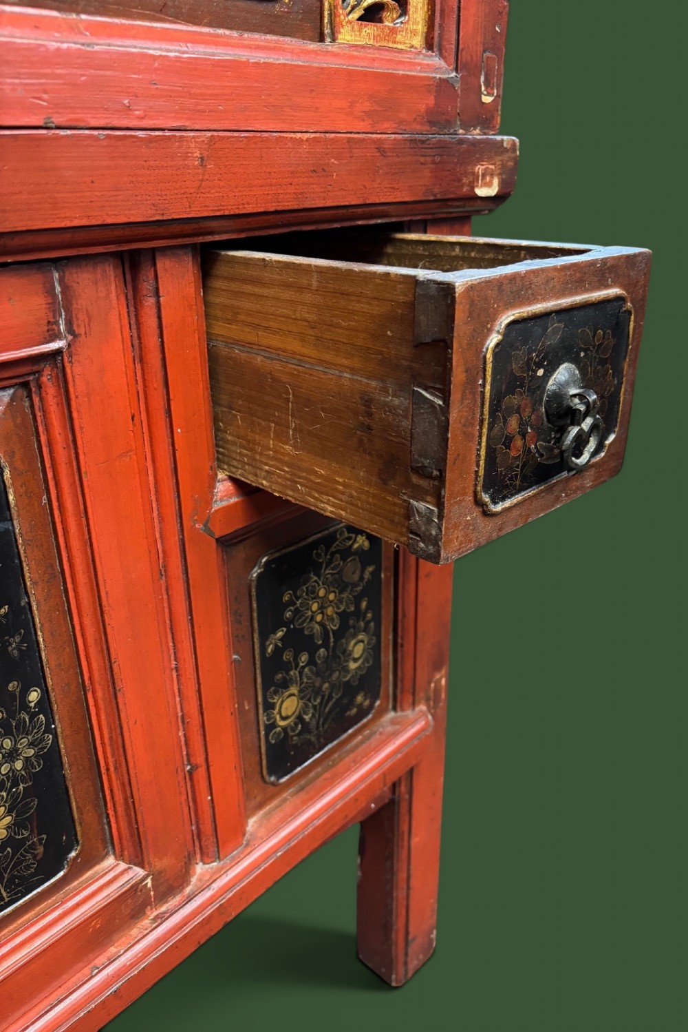 An antique Chinese tall wooden cabinet featuring red lacquered framing, gilded openwork wood carvings, black panels decorated with gold figures and floral motifs, and central brass hardware. View V