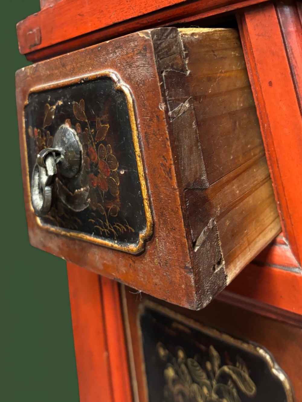 An antique Chinese tall wooden cabinet featuring red lacquered framing, gilded openwork wood carvings, black panels decorated with gold figures and floral motifs, and central brass hardware. View IX