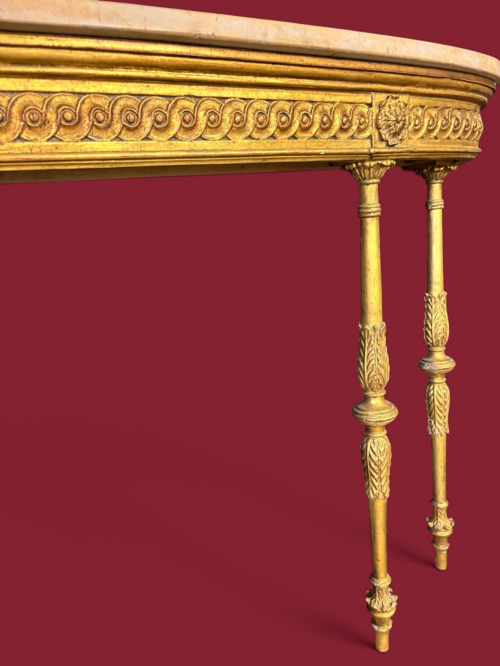 A long Neoclassical giltwood console table featuring a light marble top, a carved guilloche frieze, and slender turned legs decorated with acanthus leaf carving. View II
