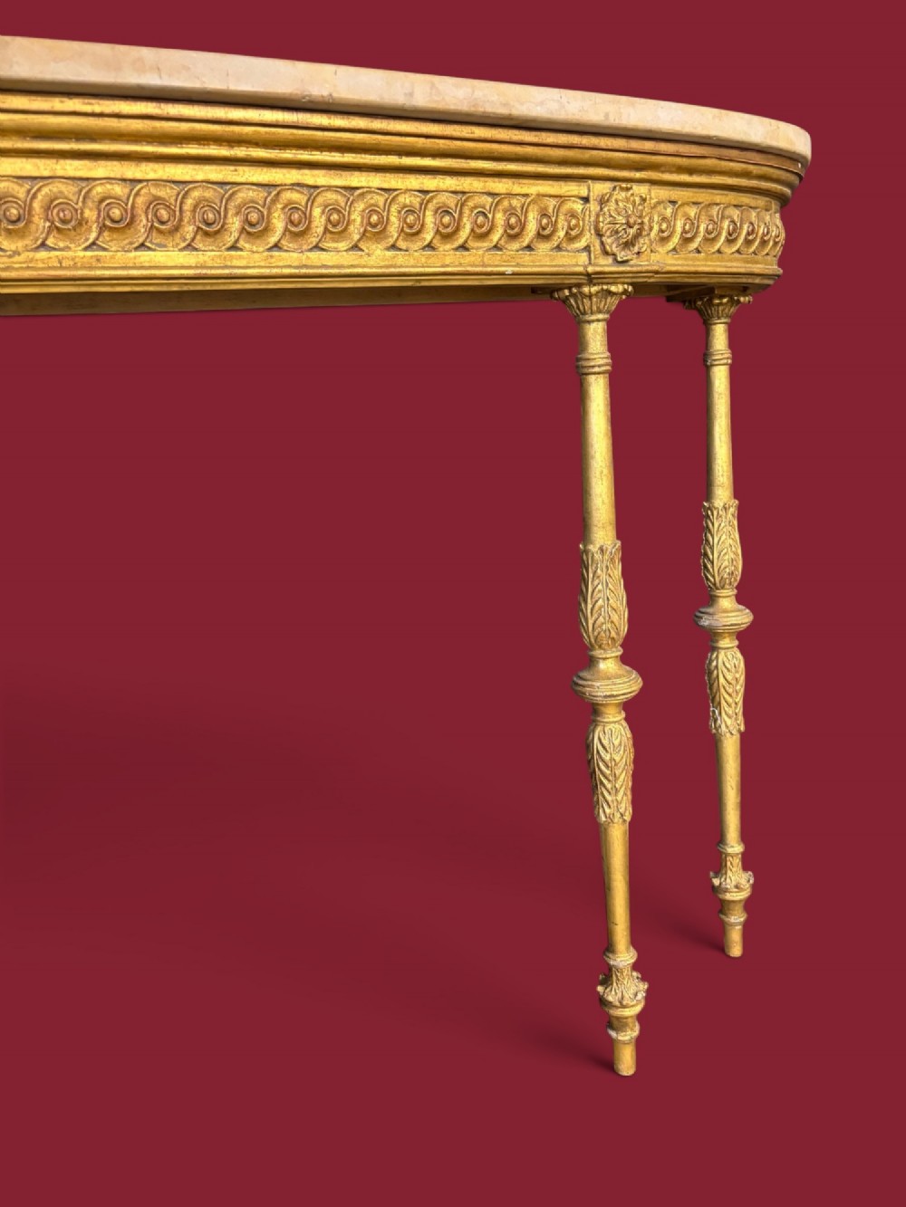 A long Neoclassical giltwood console table featuring a light marble top, a carved guilloche frieze, and slender turned legs decorated with acanthus leaf carving. View III