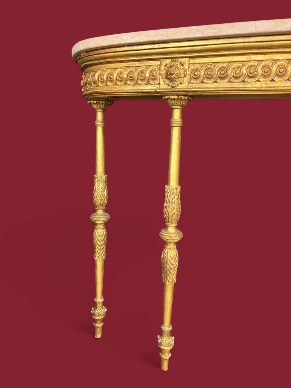 A long Neoclassical giltwood console table featuring a light marble top, a carved guilloche frieze, and slender turned legs decorated with acanthus leaf carving. View IV