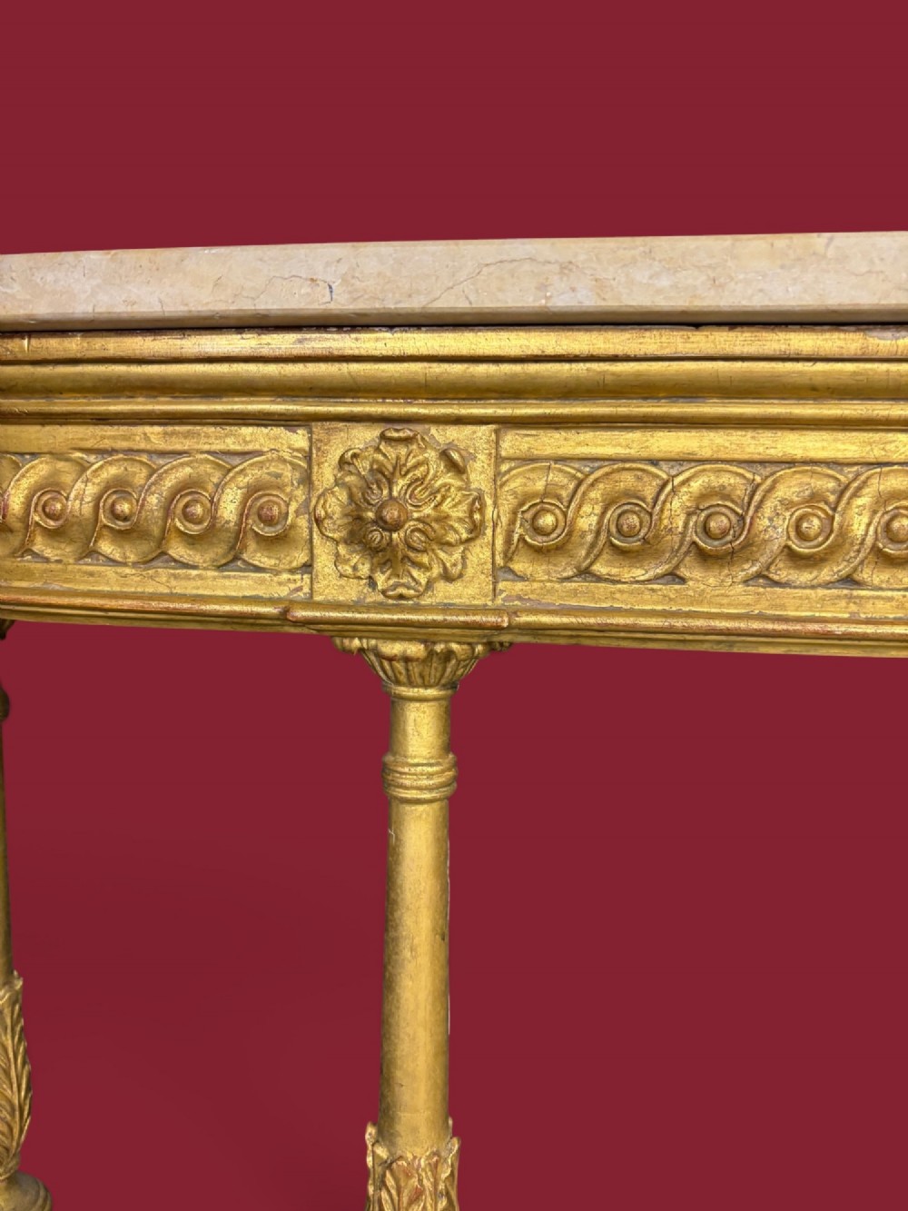 A long Neoclassical giltwood console table featuring a light marble top, a carved guilloche frieze, and slender turned legs decorated with acanthus leaf carving. View V
