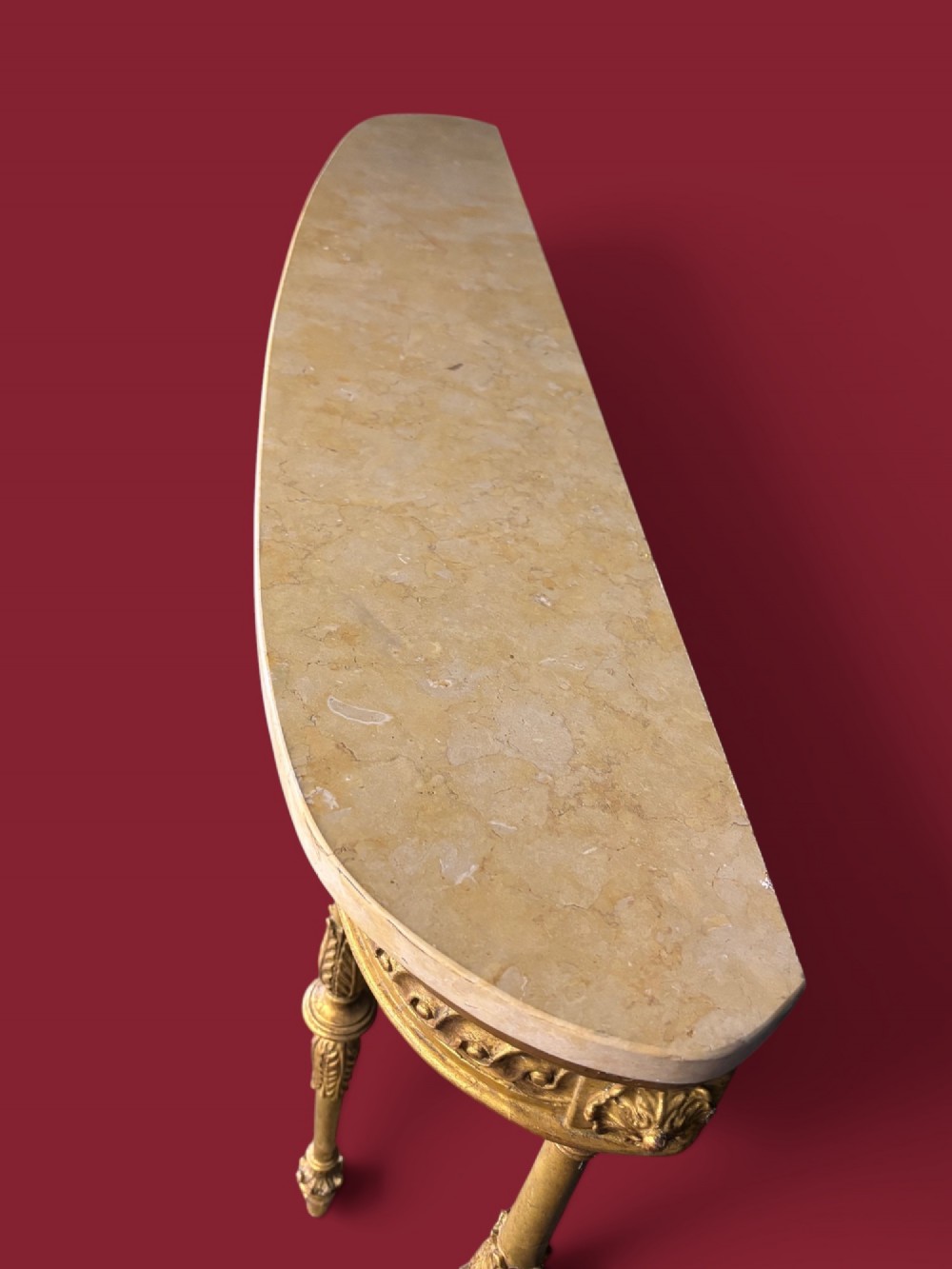 A long Neoclassical giltwood console table featuring a light marble top, a carved guilloche frieze, and slender turned legs decorated with acanthus leaf carving. View VII