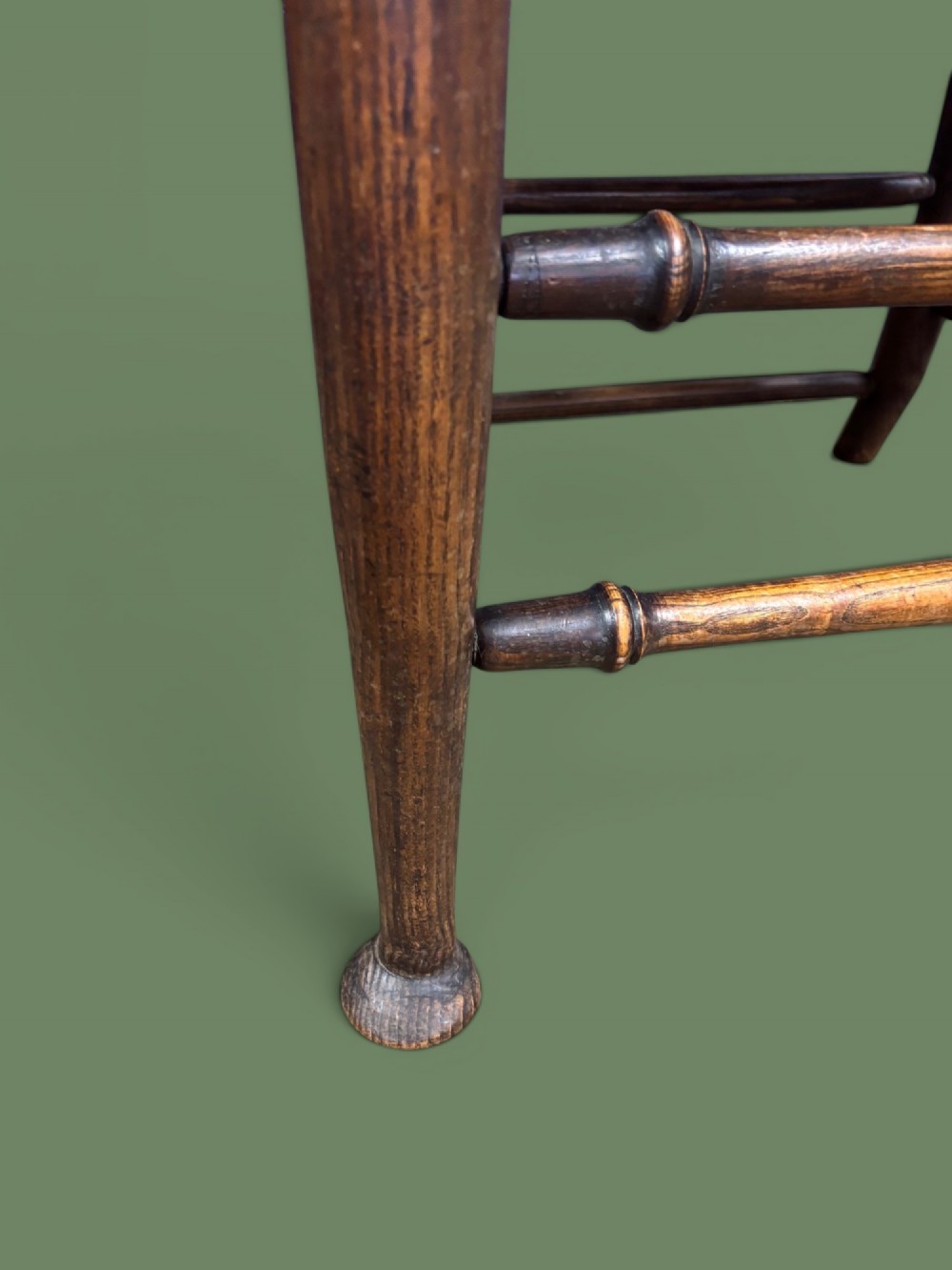 An antique elm ladderback armchair featuring six shaped horizontal slats, curved armrests, and a woven rush seat. View VII