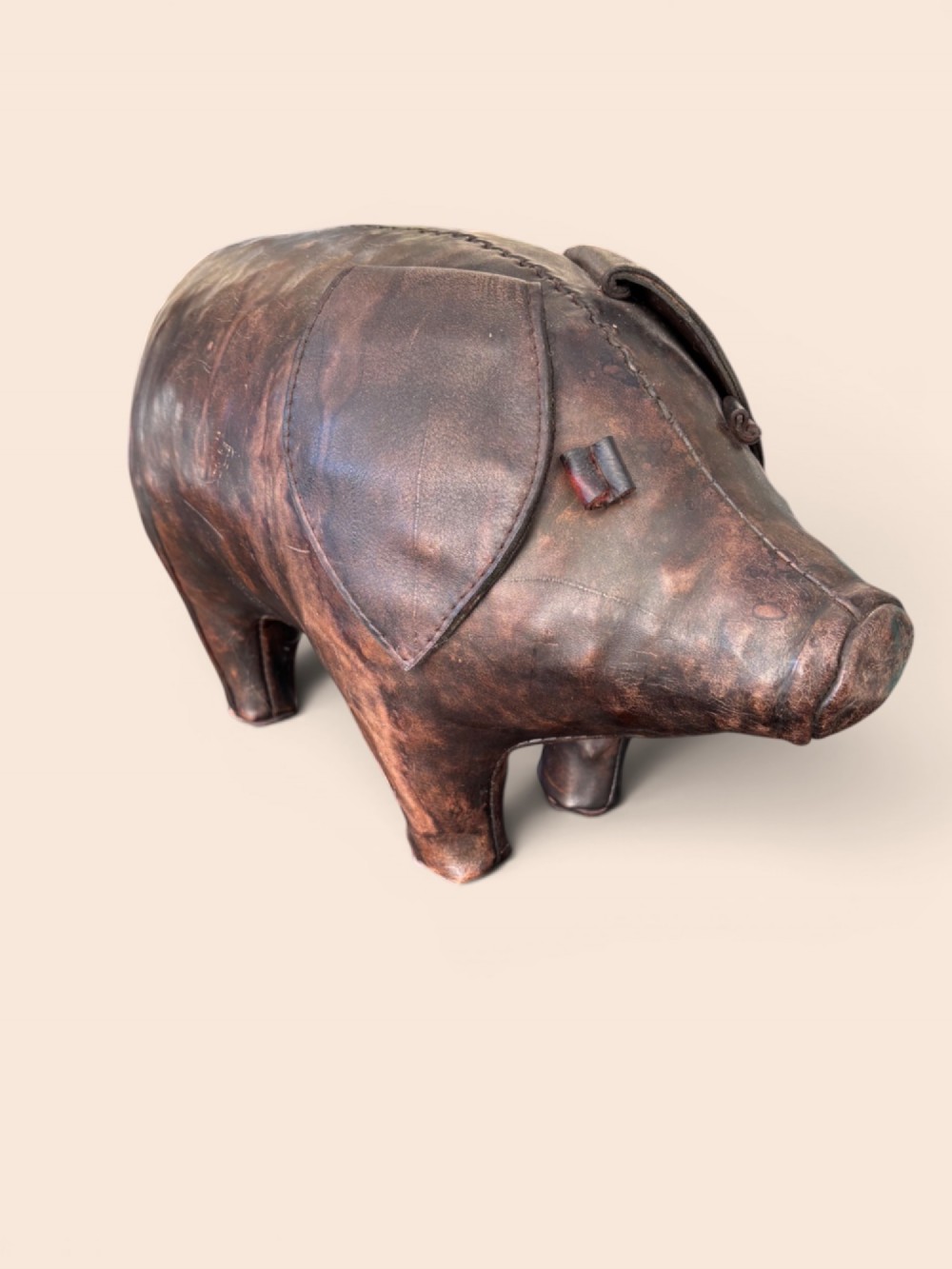 A handcrafted dark brown leather footstool shaped in the form of a pig with stitched panel detailing.