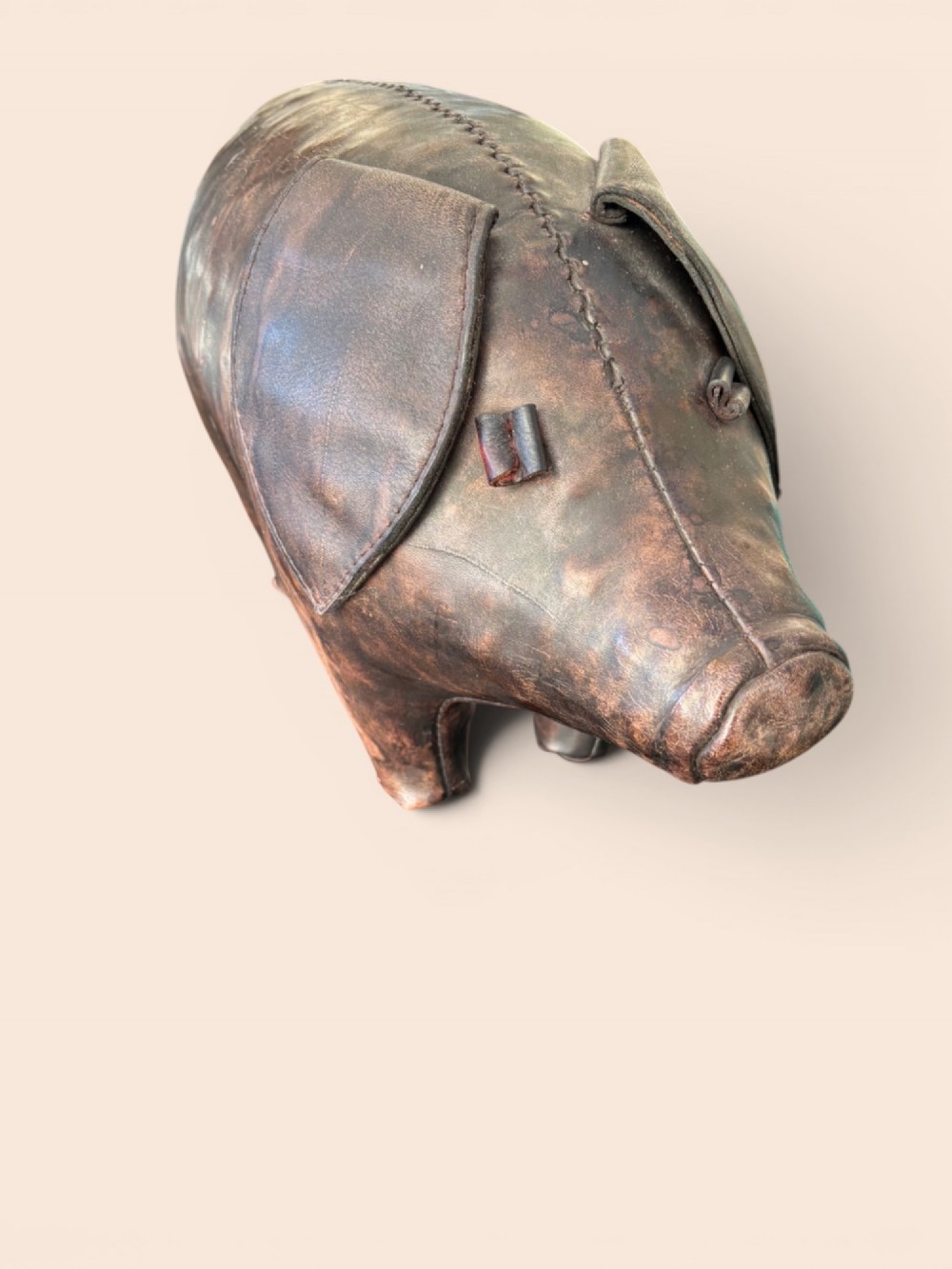 A handcrafted dark brown leather footstool shaped in the form of a pig with stitched panel detailing. View II