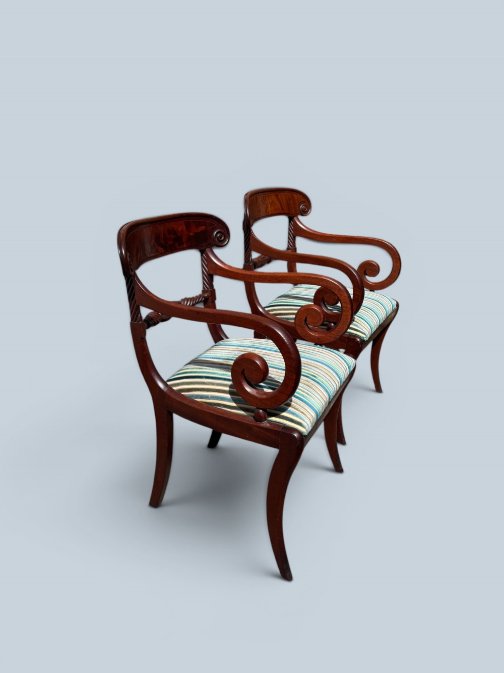 A pair of antique Regency mahogany armchairs featuring curved scroll arms, striped velvet seats, and sabre legs. View III
