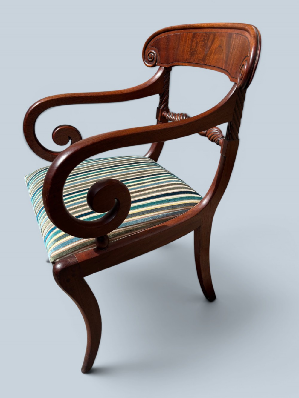 A pair of antique Regency mahogany armchairs featuring curved scroll arms, striped velvet seats, and sabre legs. View V