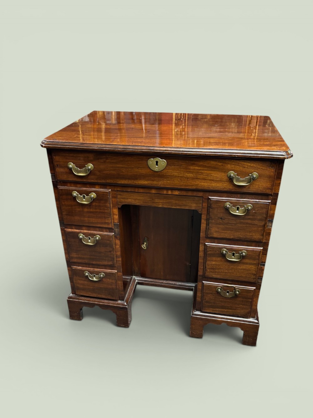 A Georgian mahogany kneehole desk with multiple drawers, brass swan-neck handles, a central recessed cupboard, and bracket feet.