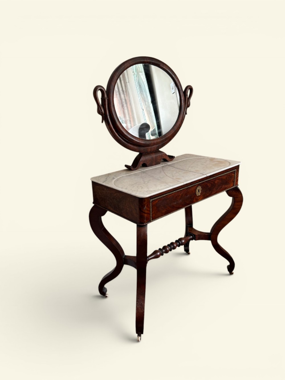 An antique dark wood dressing table featuring a swivel oval mirror, a white marble surface, S-curved legs on casters, and a central drawer.
