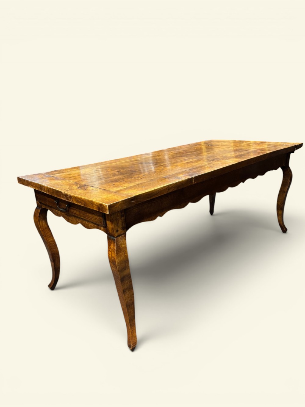 A long French farmhouse fruitwood dining table featuring curved cabriole legs, a scalloped apron, and an end drawer with an iron pull handle.