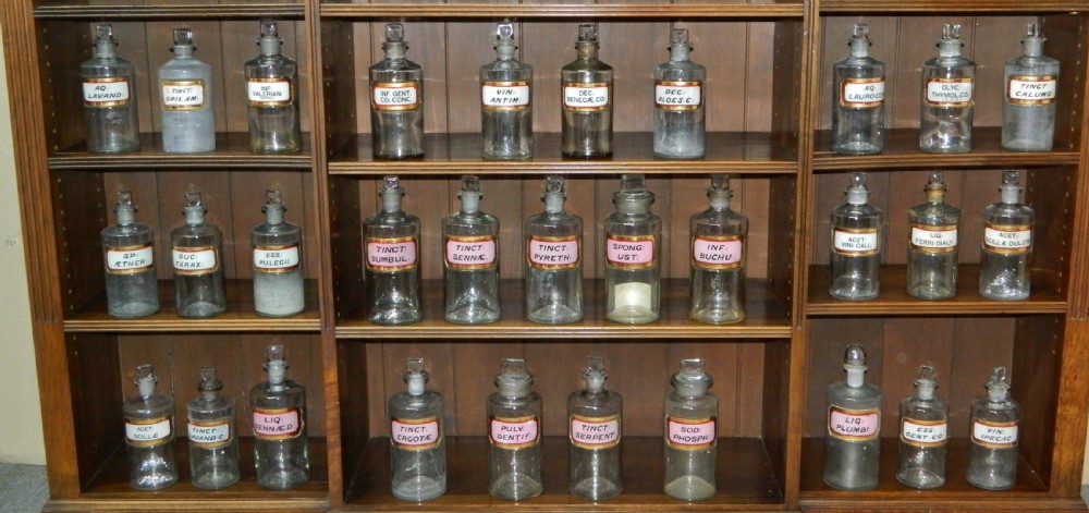 A set of twenty-nine clear glass Victorian apothecary jars with ground glass stoppers and gilt-bordered Latin paper labels.