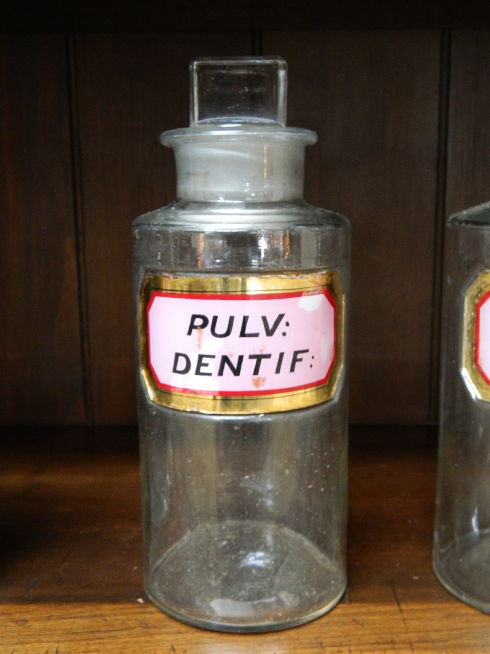 A set of twenty-nine clear glass Victorian apothecary jars with ground glass stoppers and gilt-bordered Latin paper labels. View V