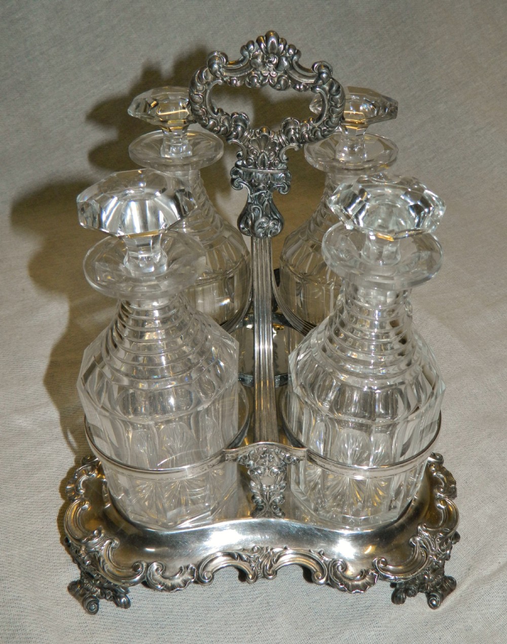 A Victorian silver-plated decanter stand featuring a central foliate handle and four matching cut-glass decanters with faceted stoppers.
