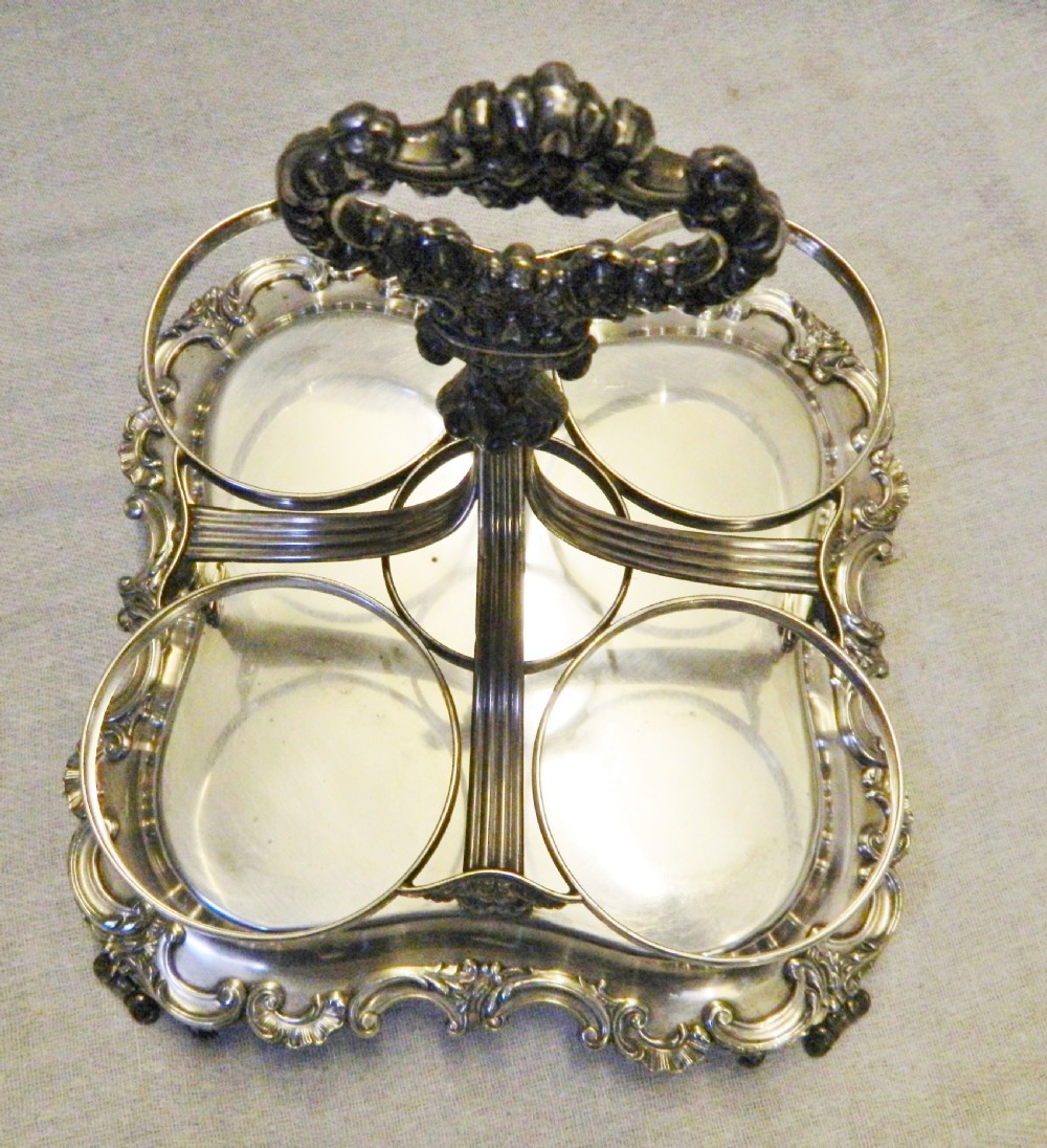 A Victorian silver-plated decanter stand featuring a central foliate handle and four matching cut-glass decanters with faceted stoppers. View VI