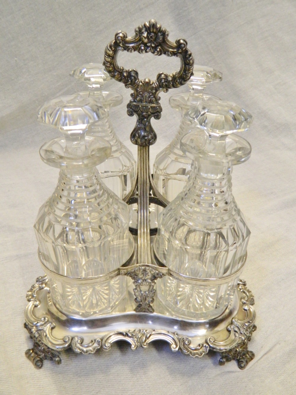 A Victorian silver-plated decanter stand featuring a central foliate handle and four matching cut-glass decanters with faceted stoppers. View VIII