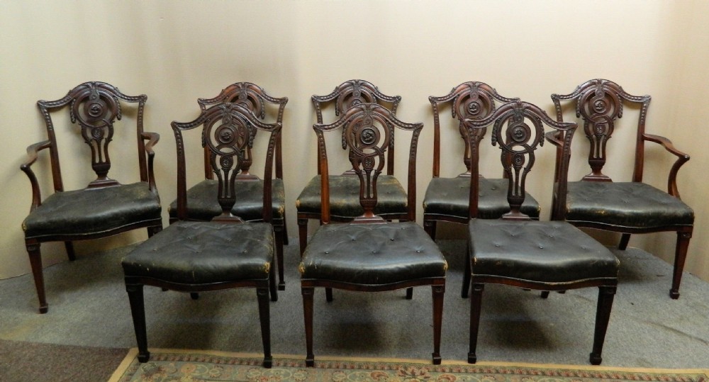 A set of eight dark mahogany dining chairs including six side chairs and two carver armchairs with intricate carved splat backs and buttoned dark leather seats.