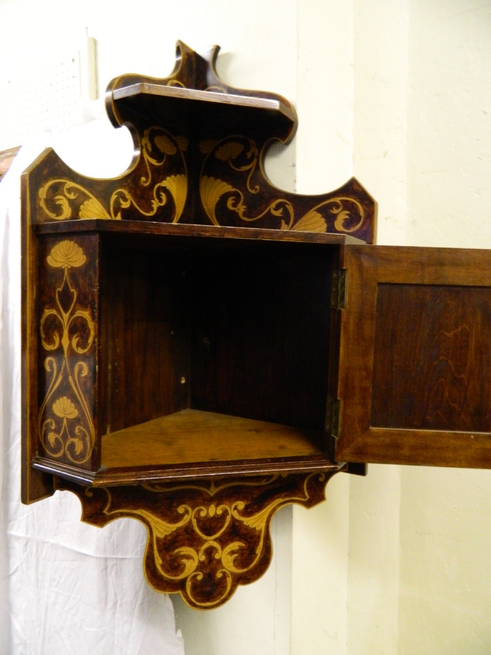 A dark wood hanging wall cabinet decorated with intricate floral light-wood marquetry inlay, featuring a single door and a shaped decorative gallery. View IV