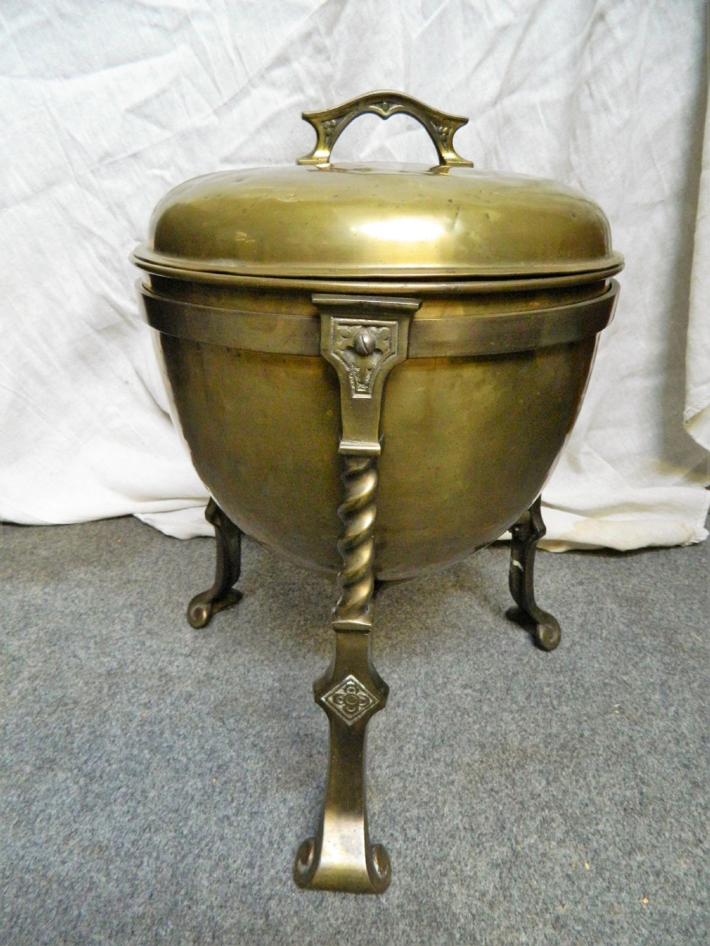 An Arts and Crafts period brass coal bin featuring a domed removable lid, top handle, and three twisted spiral legs on tripod feet.