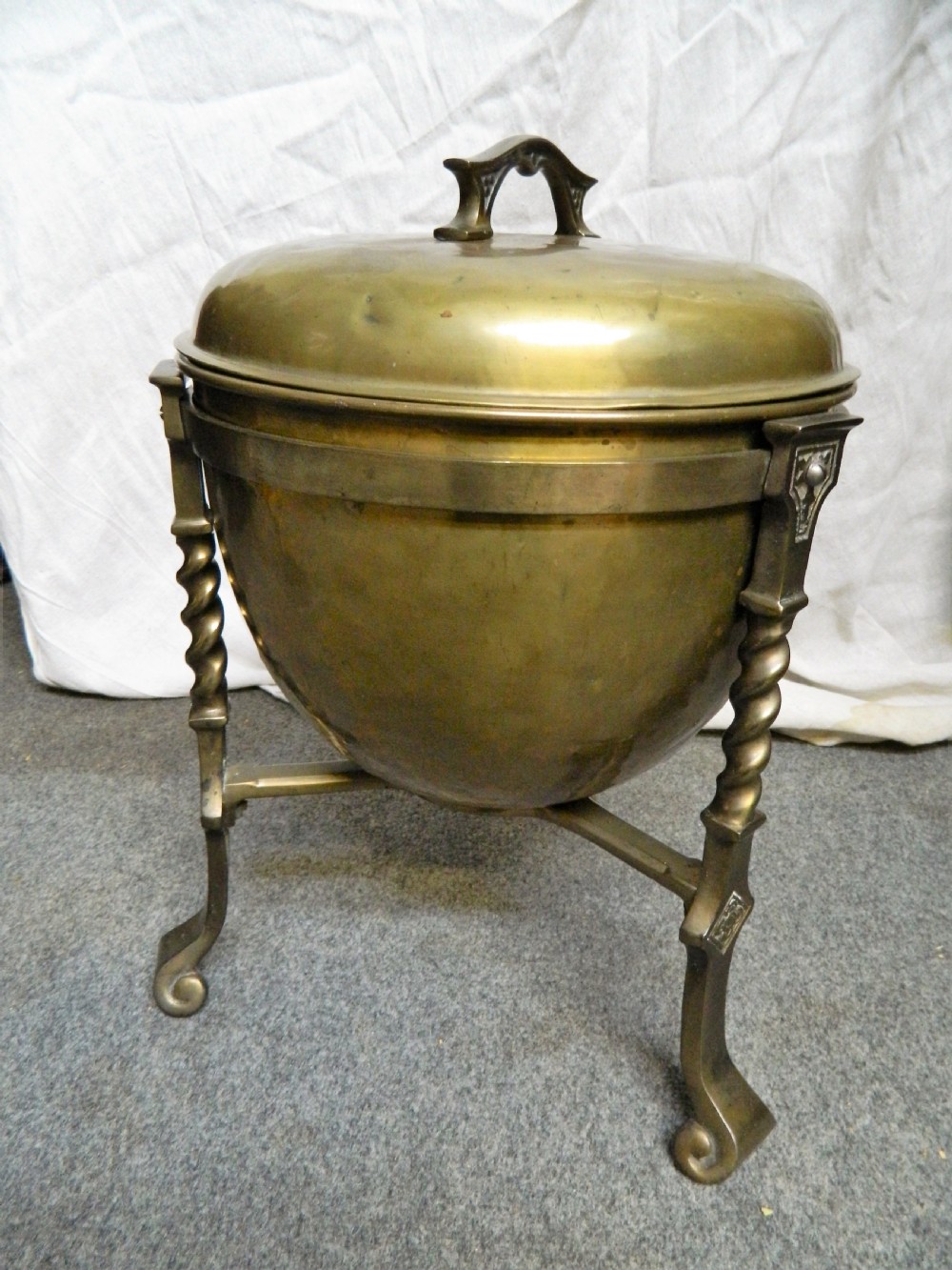 An Arts and Crafts period brass coal bin featuring a domed removable lid, top handle, and three twisted spiral legs on tripod feet. View VI