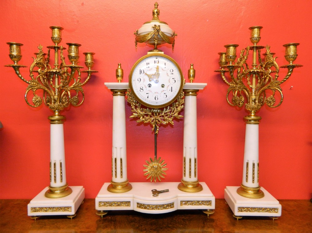 A French Neoclassical white marble and gilt ormolu portico mantel clock flanked by two matching five-light candelabra.