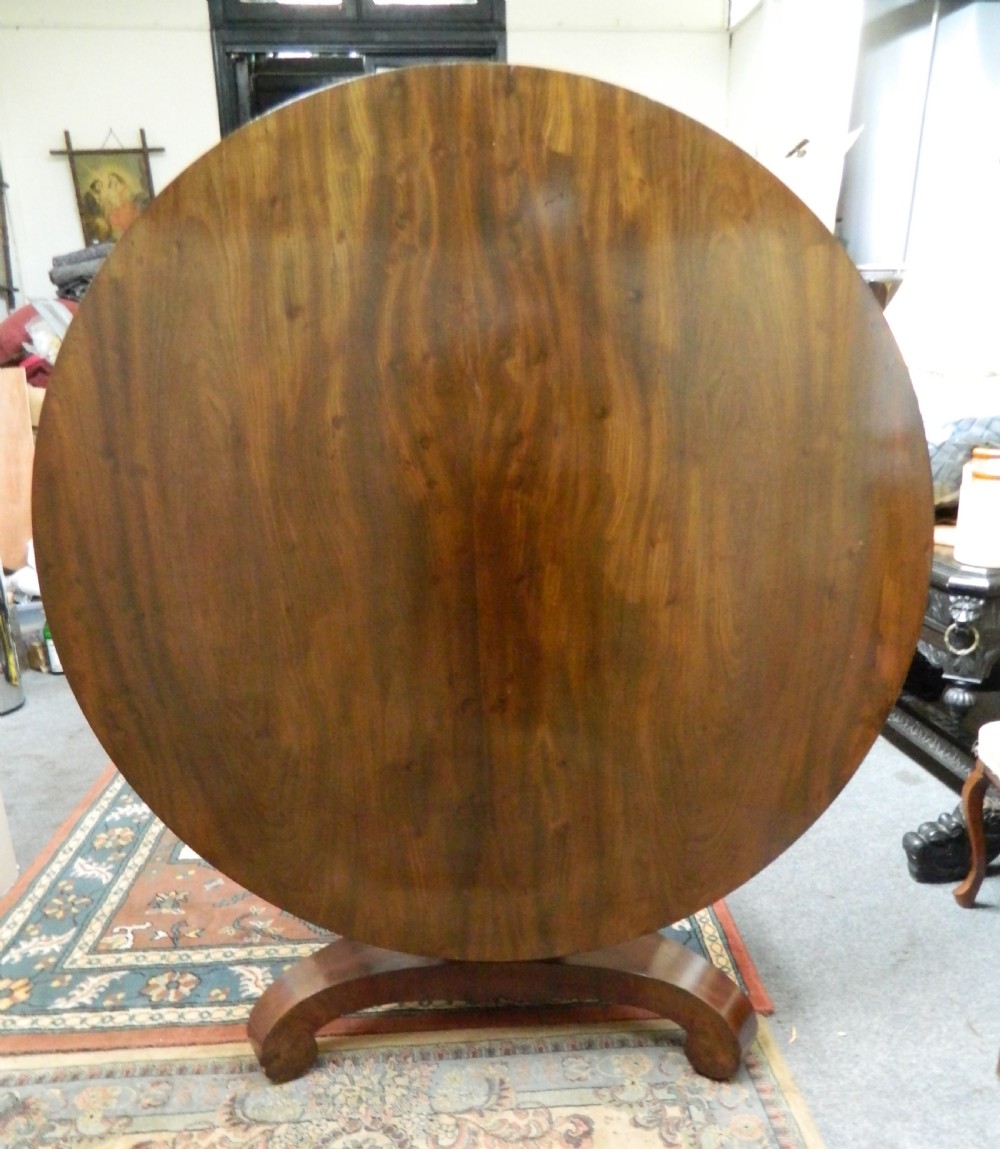 A large circular mahogany tilt-top table shown with its top tilted vertically above a curved pedestal base.
