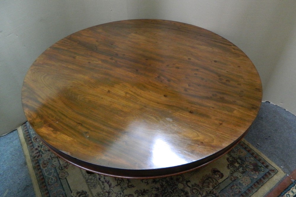 A large circular mahogany tilt-top table shown with its top tilted vertically above a curved pedestal base. View VI