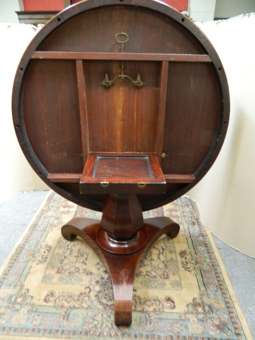 A large circular mahogany tilt-top table shown with its top tilted vertically above a curved pedestal base. View VII