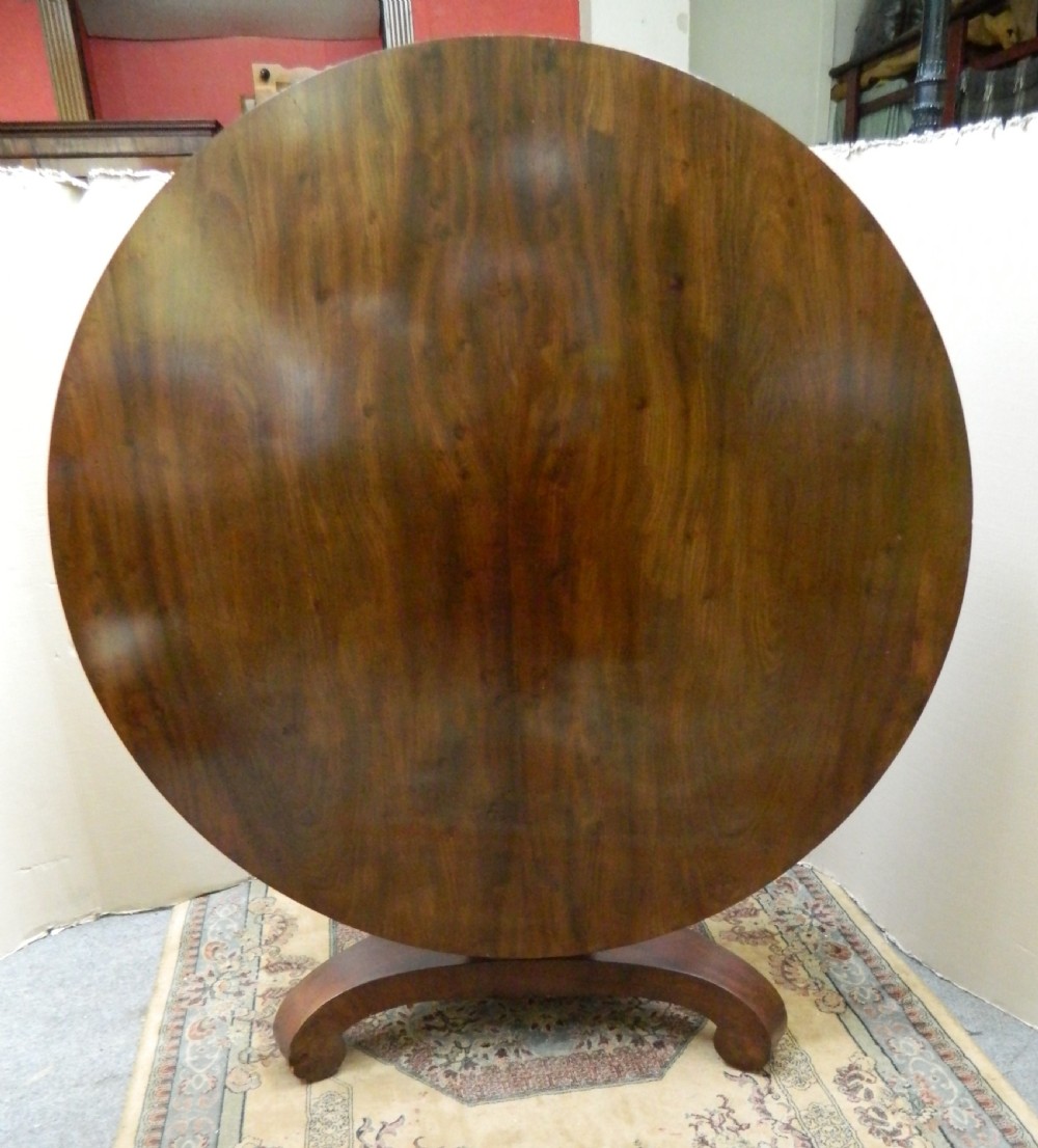 A large circular mahogany tilt-top table shown with its top tilted vertically above a curved pedestal base. View VIII