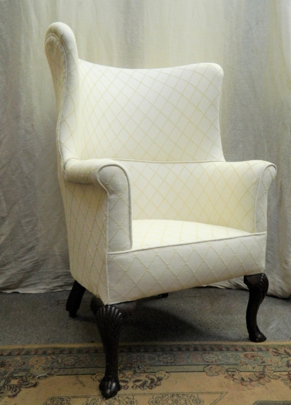A Georgian barrel back armchair upholstered in a cream diamond-patterned fabric, supported by dark mahogany cabriole legs with shell-carved knees and ball and claw feet.