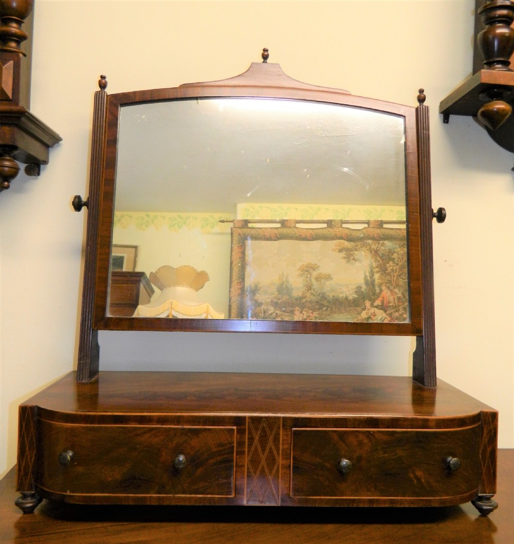 An antique mahogany toilet mirror featuring a swivelling arched glass frame mounted on a base with two inlaid drawers.