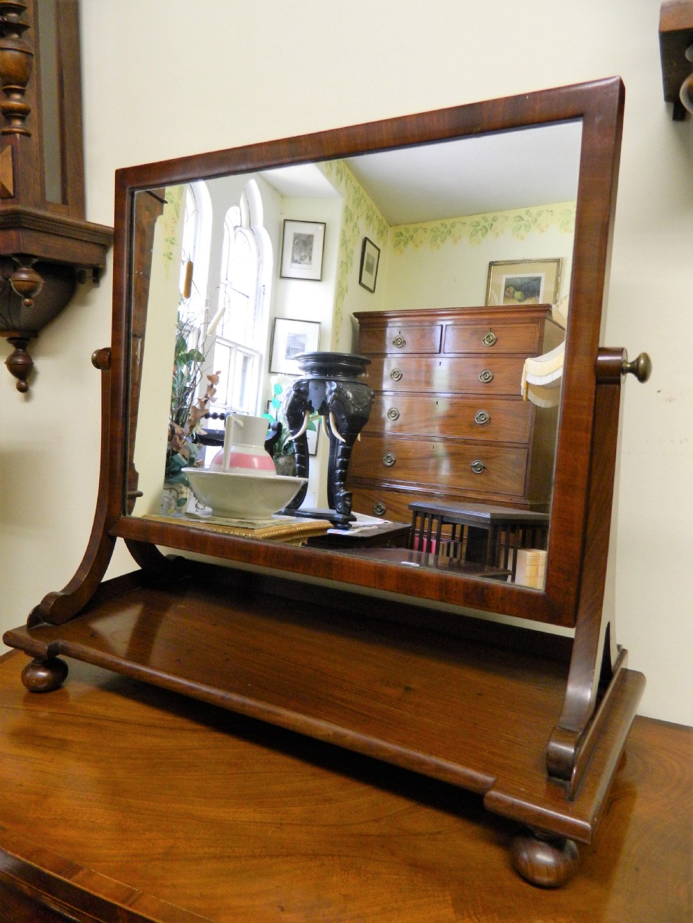 An antique mahogany rectangular toilet mirror supported on curved upright arms above a rectangular plinth base with bun feet.