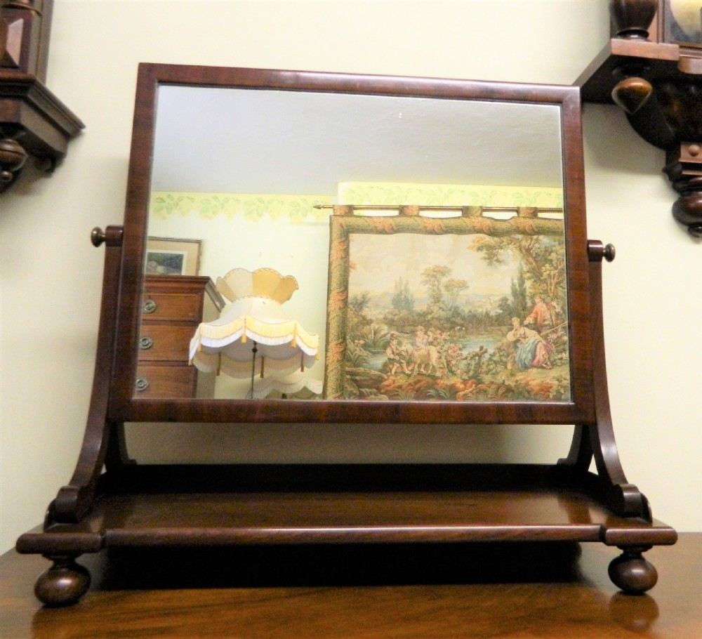 An antique mahogany rectangular toilet mirror supported on curved upright arms above a rectangular plinth base with bun feet. View II