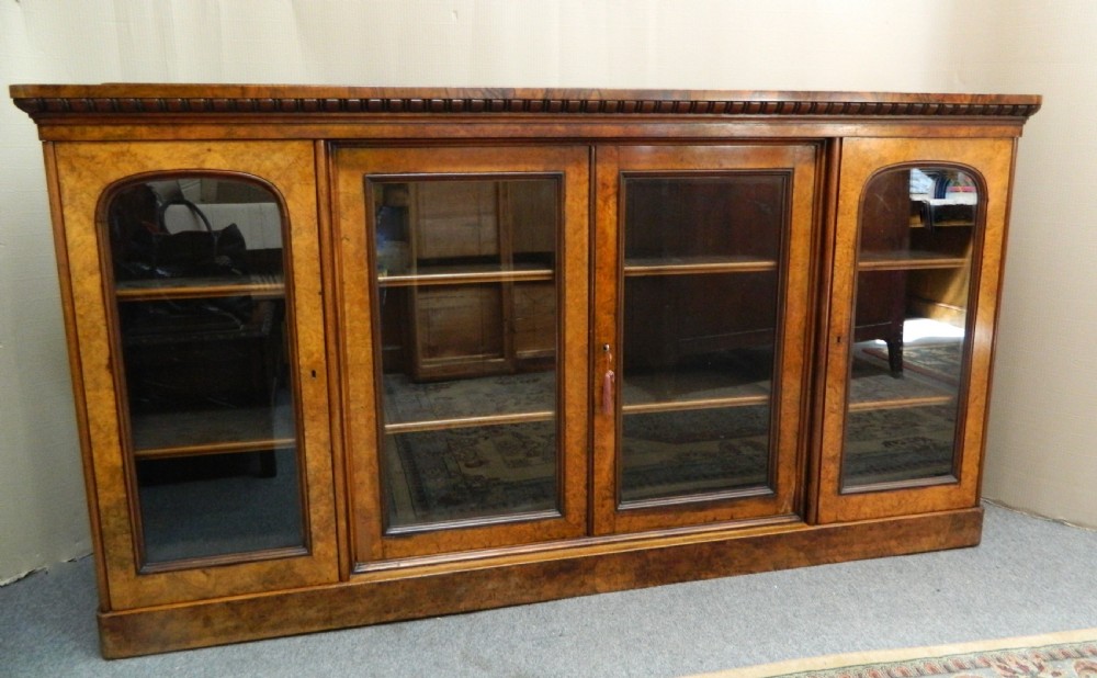 A large Victorian burr walnut bookcase featuring four glass-panelled doors, detailed wood grain patterning, and a solid plinth base.