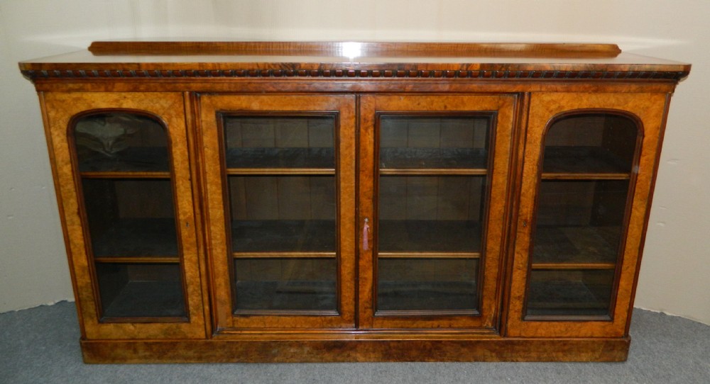 A large Victorian burr walnut bookcase featuring four glass-panelled doors, detailed wood grain patterning, and a solid plinth base. View III